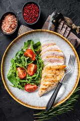 Sliced chicken breast fillet steak with green salad in a plate. Black background. Top view