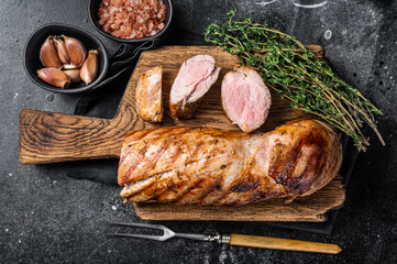 BBQ roasted pork tenderloin fillet meat on wooden board with herbs. Black background. Top view