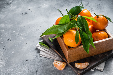 Organic Tangerines, mandarins with green leaves in wooden box. Gray background. Top view. Copy space