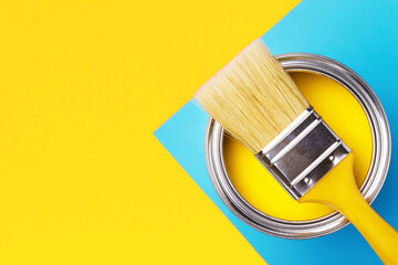 Can of yellow paint with brush on yellow and blue background. Top view, redecorating concept.