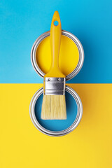 Can of yellow paint with brush on yellow and blue background. Top view, redecorating in ukrainian flag colors.