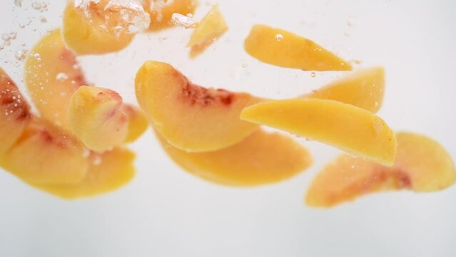 Peach Slices Falling into Water in Slow Motion on White Background Isolated. Fruits Splashing into Clear Water. Healthy Food Concept. Macro