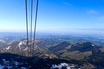 Aerial view with Mountains and midland in the background seen from Säntis peak at Alpstein Mountains on a sunny spring day. Photo taken April 19th, 2022, Säntis, Switzerland.