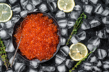 Salty Red caviar in steel plate on ice. Black background. Top view. Copy space