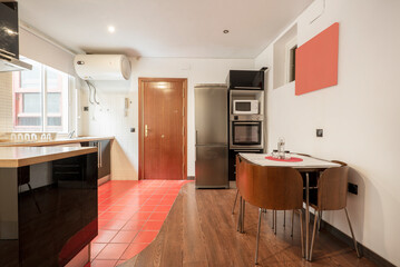 Kitchen with designer dining table with wooden and metal chairs and column with stainless steel appliances and refrigerator