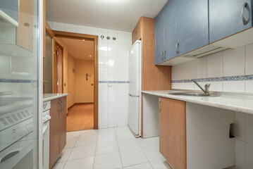 kitchen with lower furniture in wood, upper blue, similar marble countertop and integrated white appliances to match the tiles and the border