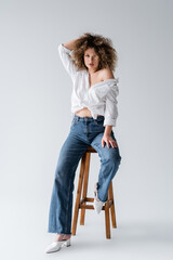Trendy model in blouse sitting on chair on white background. - obrazy, fototapety, plakaty