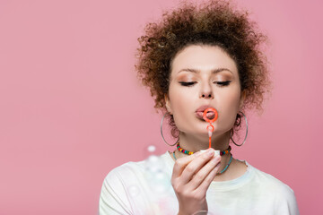 Curly woman blowing soap bubbles isolated on pink.