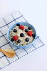 Oatmeal on water with berries in a blue plate on a white background. Diet breakfast for weight loss