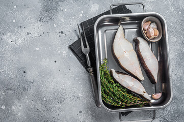 Fresh steak of raw fish halibut in kitchen tray with herbs. Gray background. Top view. Copy space