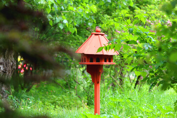 Cute red birdhouse in the beautiful park. Beautiful spring or summer day. Selective focus.