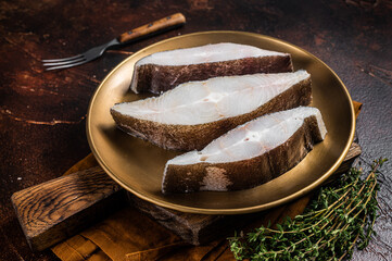 Sliced halibut fish, raw steaks on plate with thyme. Dark background. Top view - obrazy, fototapety, plakaty