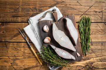 Atlantic halibut fish, raw steaks on wooden board with herbs. Wooden background. Top view - obrazy, fototapety, plakaty