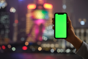 Fototapeta na wymiar hand showing green screen phone with blur colorful Shanghai city bokeh background