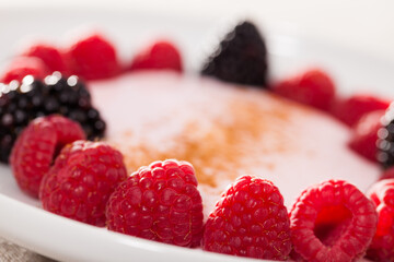 raspberries and blackberries laid out on a white plate in circle with yogurt and cinnamon