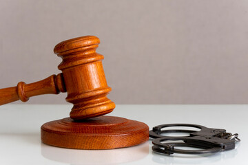 Wooden judge's gavel and police handcuffs on a gray background, copy space.