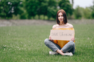 girl Sits on the green grass and asks to save Ukraine. War in the 21st century.