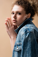 Portrait of woman in denim jacket doing praying hands isolated on beige.
