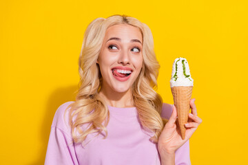 Photo of funny positive lady hold ice cream tongue lick teeth look empty space isolated on yellow color background - obrazy, fototapety, plakaty