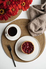 Breakfast with dessert pie on plate, cup of coffee on rattan rug. Table decorated with red flowers bouquet, linen blanket. Flat lay, top view