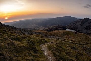 A mountain trail leading towards a wild camping tent at sunset