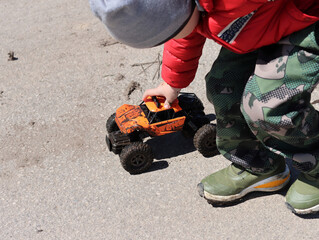 A boy in a red jacket plays with an orange toy monster truck © MIKHAIL BATURITSKII	