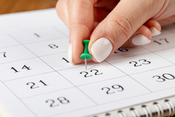a female hand with a beautiful manicure holds a green pushpin to mark the date on the calendar 22 day