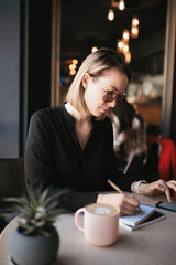 A woman works remotely, looking for information on her smartphone and making notes in a notebook.