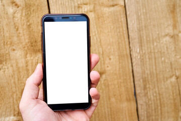 A man's hand holds a mobile phone against a background of wood texture. Phone template with white screen