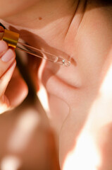 A woman applies oil to body. A drop of essential oil drips from a pipette onto a woman's...