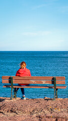 one single woman alone sitting on a bench watching the sea horizon