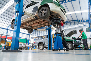 Naklejka premium Auto mechanic working in Car repair station paved with epoxy floor and electric lift for a car that comes to change the engine oil in the background of Car repair center with epoxy floors.