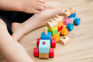 Boy sitting on the floor and playing with wooden colorful block train. Pre-school employment. Montessori concept. Brain and coordination exercise. Careless childhood.