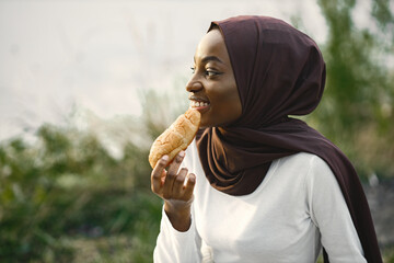 Portrait of a muslim woman sitting near the river and eating croissant