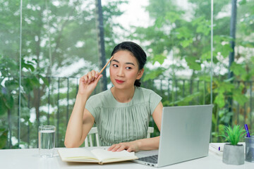 Business Asian young woman working with computer laptop holding pen and thinking to get ideas and requirement