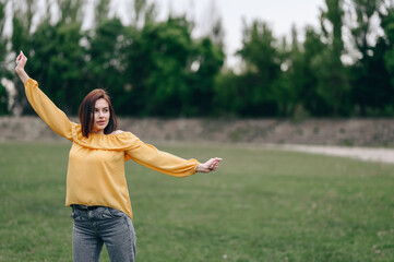 A girl in a yellow blouse spreads her arms to the side and looks into the distance