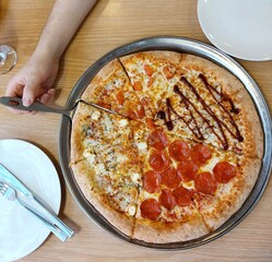 close up of pizza.Pizza on round metal platter.A hand is holding a slice of pizza.Pepperoni,cheese,salami,bacon.