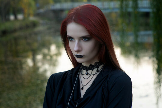 beautiful fashionable young girl witch model stands outdoors in the forest in autumn by the river, pale, vampire, goth