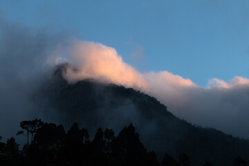 Sea of clouds on top of the mountain, illuminated by sunset light and silhouette of forest, mystery scene, Teresópolis, Rio de Janeiro, Brazil