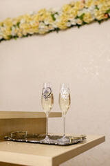 Glass glasses of the bride and groom with champagne are on the table for the wedding ceremony. Glasses of champagne for the newlyweds on a tray