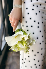 Wedding bouquet of callas in the hands of the bride close-up. Beautiful wedding bouquet of callas tied with a silk ribbon. Vertical photo of the bride's wedding bouquet