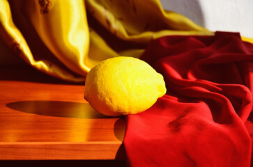 Minimalistic lemon still life with red and yellow silk fabric.