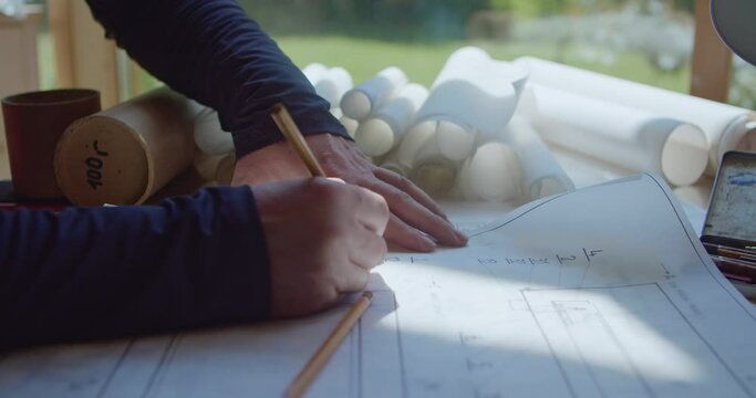 The hands of the architect-designer lie over the construction drawing and write notes in pencil