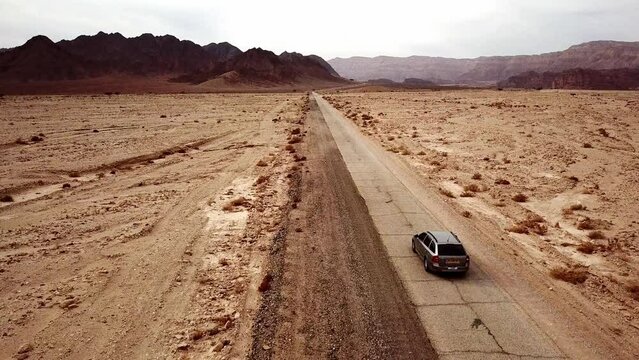 Passenger car drives left-handed on the torn dry dirt road between the red canyon in the dry Timna Park in the Negev Desert in southern Israel on a sunny day. Drone following shot