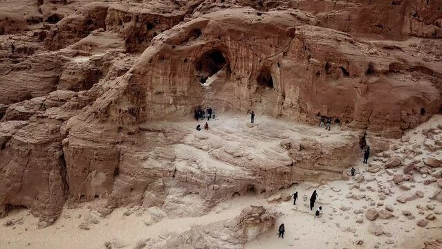 Group of tourists take pictures and enjoy the view at The Arches in the dry Timna Park in the red canyon in the Negev desert in southern Israel. High angle drone dolley shot