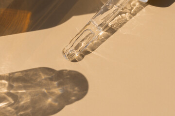 close up of pipette with pouring liquid serum with golden bottle and shadows