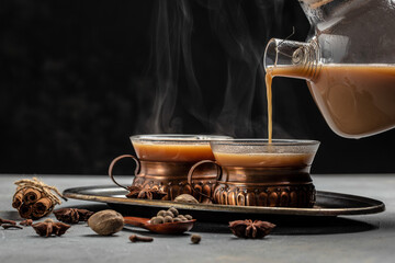 Two mugs of masala tea. Hot indian masala chai tea with milk and spices in a glass glass on dark background. place for text - obrazy, fototapety, plakaty