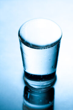 Glass filled to the brim with water in blue monochrome.