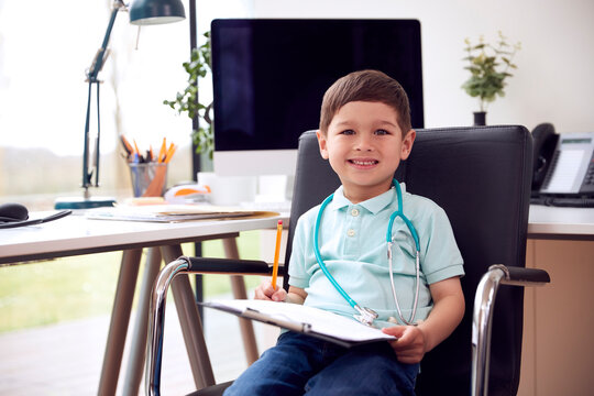 Portrait Of Smiling Young Boy Sitting In Chair In Office Pretending To Be Doctor