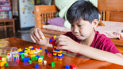 Asian boy is getting creative with assembling colorful plastic bricks into robots and planes on a wooden table happy and fun at home.Kid Creators concept.